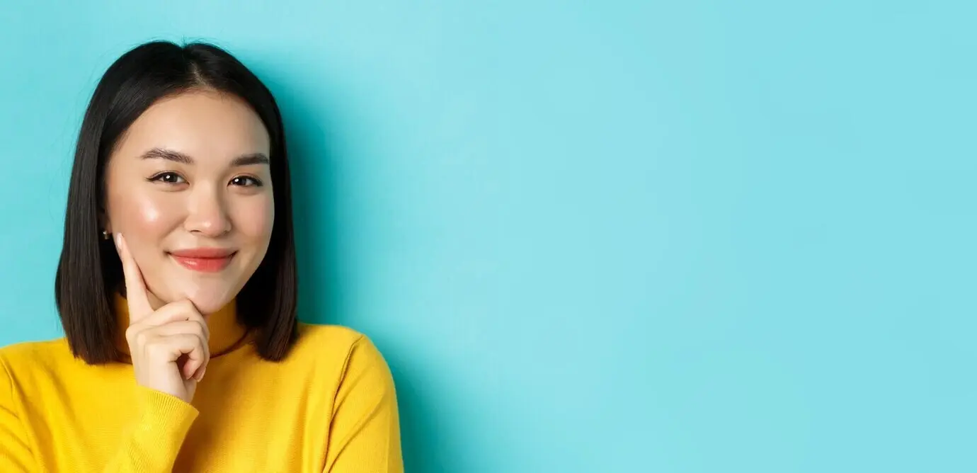 Schoonheids- en make-upconcept: close-up van een nadenkende Aziatische vrouw die tevreden in de camera kijkt en glimlacht.