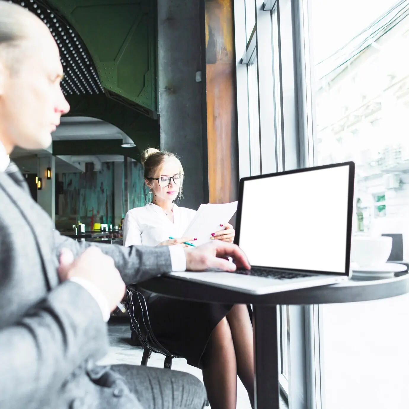 Een zakenman gebruikt een laptop terwijl zijn collega documenten doorneemt in een café.