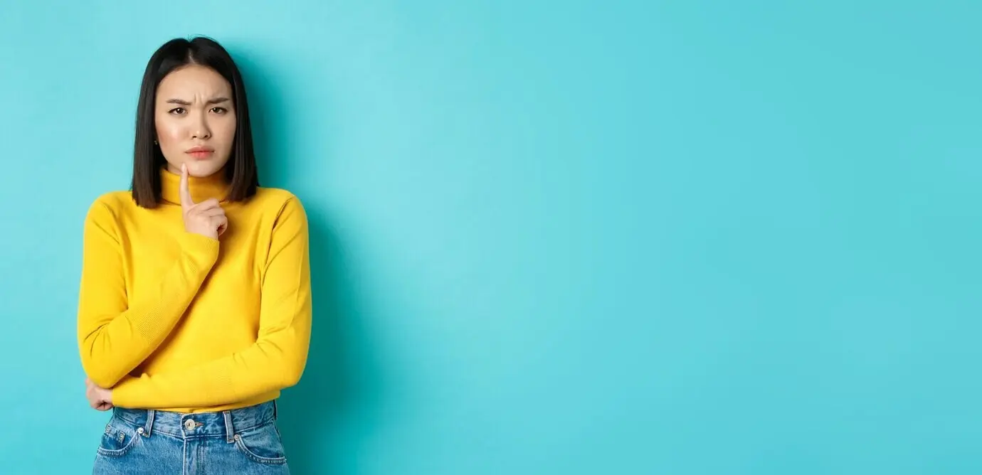 Afbeelding van een peinzende Aziatische vrouw die haar lip aanraakt en fronst, terwijl ze over iets nadenkt en probeert het te begrijpen.